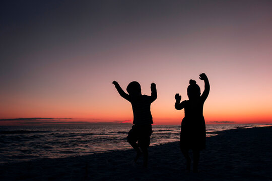 Silhouette siblings dancing at beach against sky during sunset