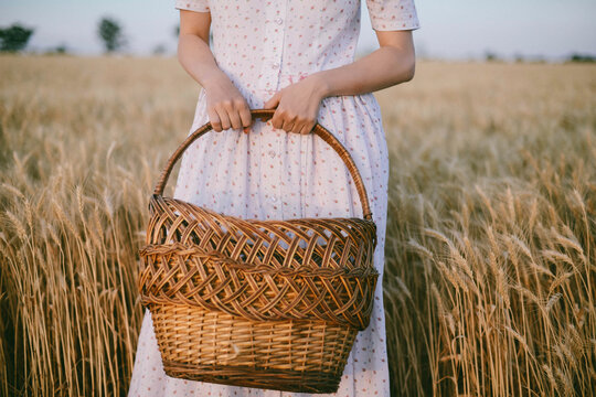 Midsection of woman holding wicker basket while standing amidst crops