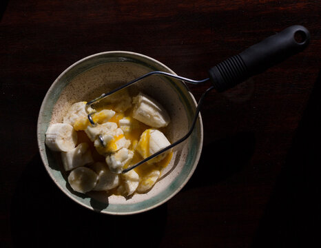 Overhead view of banana slices and eggs in bowl with masher on table