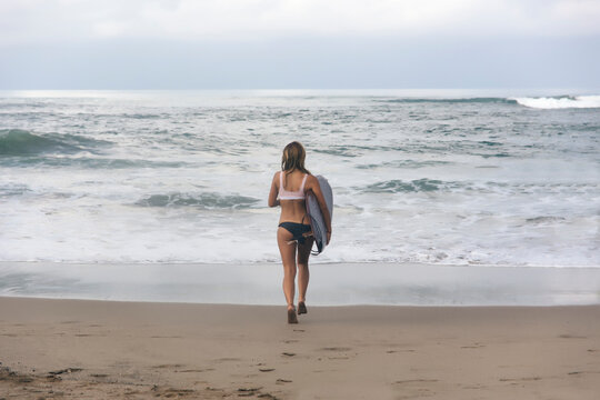 Rear view of woman carrying surfboard while running towards sea at beach