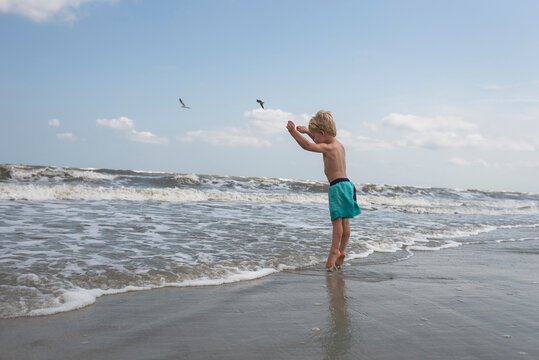 Side view of shirtless boy standing at beach against sky