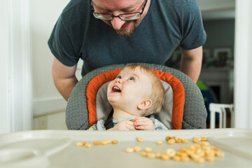 Father looking at happy son sitting on high chair