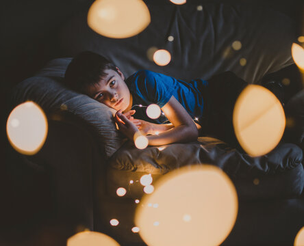 Portrait of boy with illuminated string lights lying on sofa at home