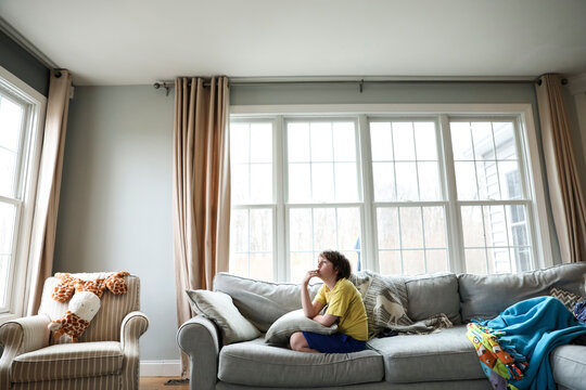 Thoughtful Boy Sitting On Sofa In Living Room At Home