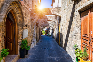 Fototapeta na wymiar Medieval arched street in the old town of Rhodes, Greece. Rhodes old town in Rhodes island in Greece. Historical streets of old town Rhodes with flowers in Rhodes, Dodecanese, Greece