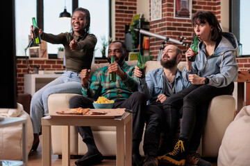 Happy friends watching football game tournament on sport tv channel, cheering in front of television to score goal on pitch. Looking at soccer match championship and drinking beer for fun.