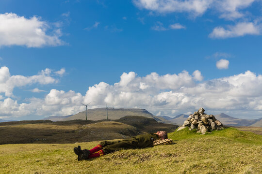Man lying on grassy field against cloudy sky