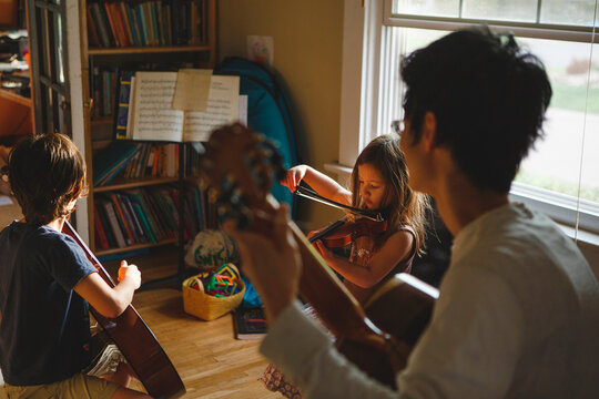 Father With Children Playing String Instruments At Home