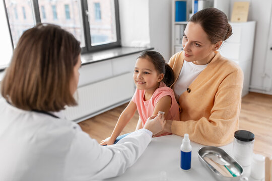 medicine, healthcare and pediatry concept - female doctor or pediatrician disinfecting arm skin of little girl patient with mother at clinic