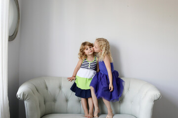 Girl kissing sister while standing on sofa by wall at home