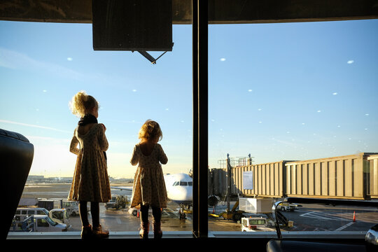 Rear view of sisters looking through window while standing at airport