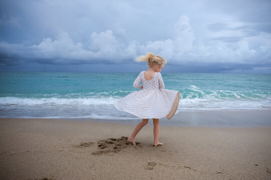 Full length of playful girl spinning at beach against cloudy sky