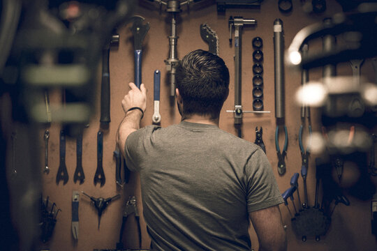 Rear view of male owner arranging work tools on pegboard at workshop