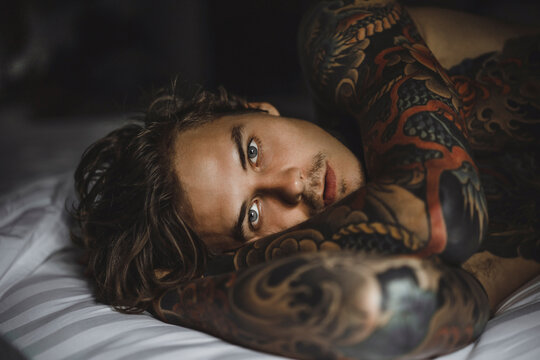 Close-up portrait of shirtless tattooed man lying on bed at home