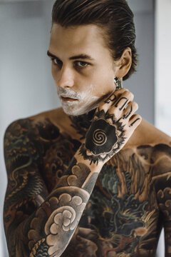 Shirtless tattooed man shaving in bathroom at home