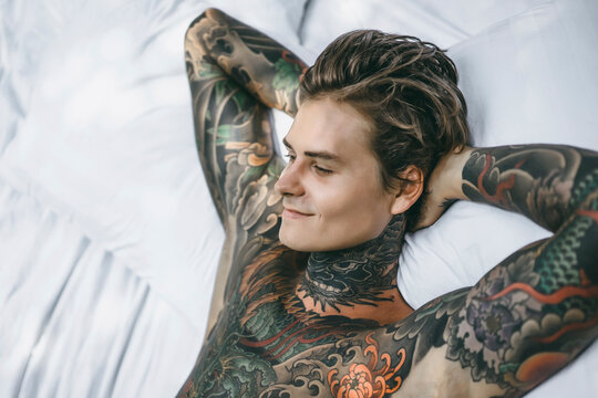 High angle view of smiling tattooed man with hands behind head lying on blanket