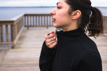 Side view of woman zipping jacket while standing on pier against sea