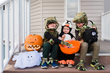 Happy siblings in Halloween costumes sitting on steps against house