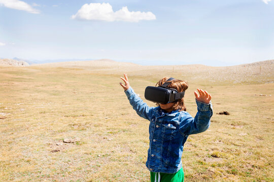 Boy looking through virtual reality simulator while standing on landscape against sky during sunny day