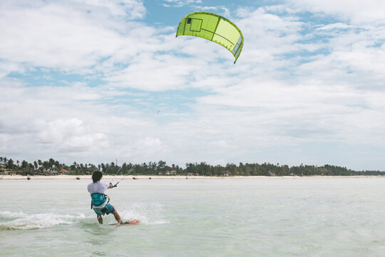 Rear view of man kiteboarding on sea against cloudy sky