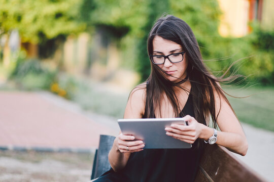 Young woman using tablet computer while sitting on bench at park