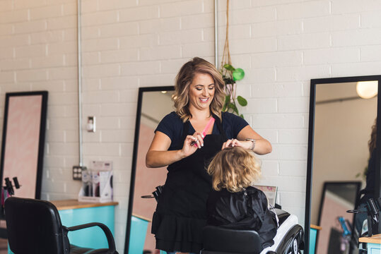 Smiling hairdresser combing girl's hair in salon