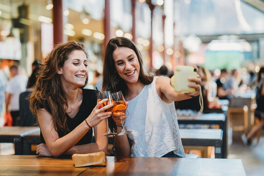 Female friends taking selfie with instant camera while toasting aperitifs in restaurant