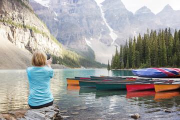 Rear view of woman photographing with mobile phone while sitting at lakeshore in Banff National Park