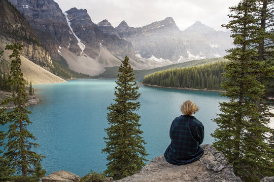 Rear view of woman looking at lake while sitting on rock in Banff National Park