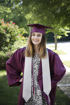 Portrait of happy woman in graduation gown standing against trees at park