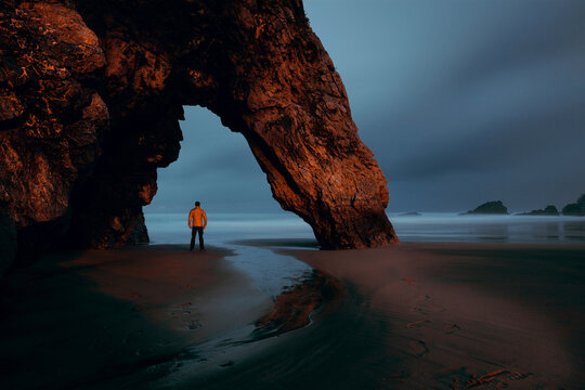 Rear view of tourist standing below natural arch at Adraga beach during twilight