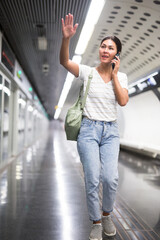 Asian woman talking on phone and waving with hand in subway station.