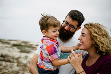 Happy parents with cute son enjoying at beach against sky
