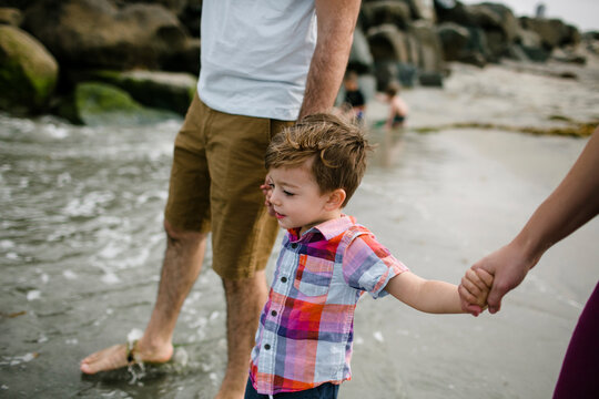 Cropped image of parents holding son's hands while walking at beach