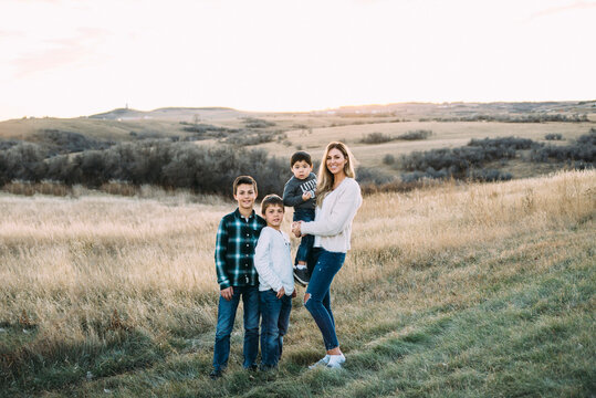 Full length portrait of mother with sons standing on field during sunset