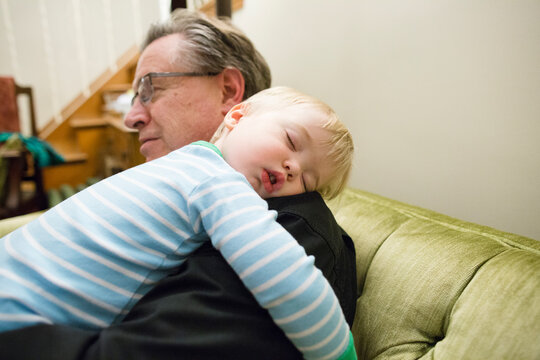 Grandfather carrying cute sleeping grandson on shoulder at home