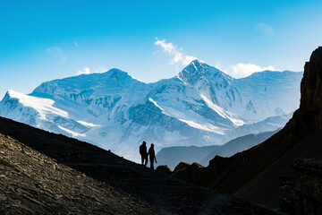 Silhouette couple holding hands while hiking on mountain against blue sky