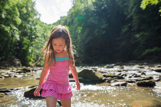 Girl walking in creek river amidst trees at forest during sunny day