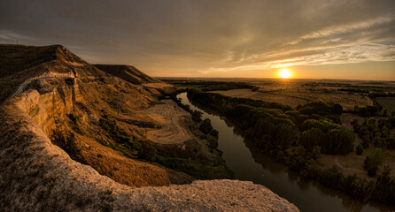 Scenic view of stream amidst mountain against cloudy sky during sunset