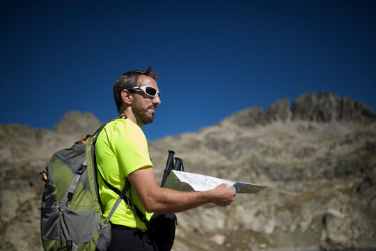 Side view of male hiker holding map while standing on mountain against clear blue sky during sunny day