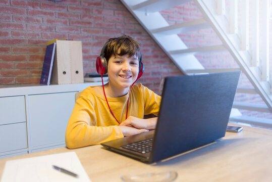 Portrait of smiling boy using headphones and laptop computer while studying at home