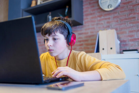 Focused boy learning using laptop computer and headphones at home