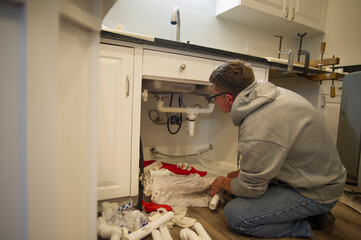 Side view of man repairing pipes in kitchen at home