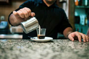 Midsection of male barista pouring milk in coffee on counter at cafe