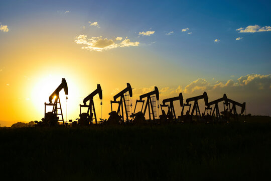 Silhouette pumpjacks on field against sky during sunset