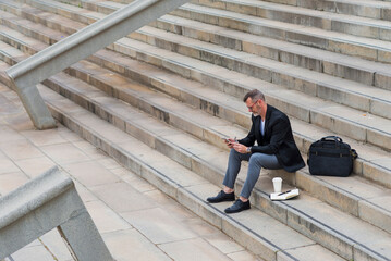 High angle view of businessman using smart phone while sitting on steps in city