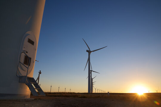 Surface level image of silhouette windmills on landscape against clear blue sky during sunset