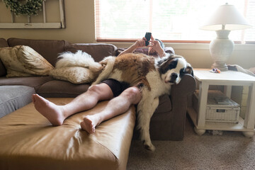 Full length of man using mobile phone while lying with Saint Bernard on couch at home