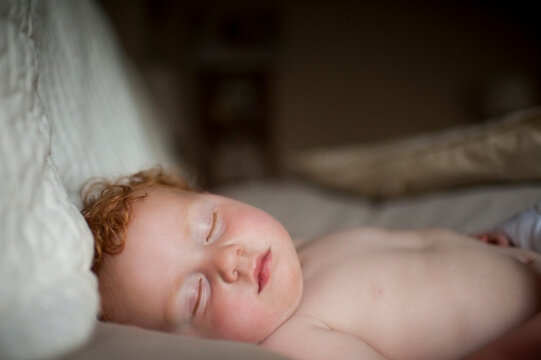 Cute shirtless baby boy sleeping on bed at home