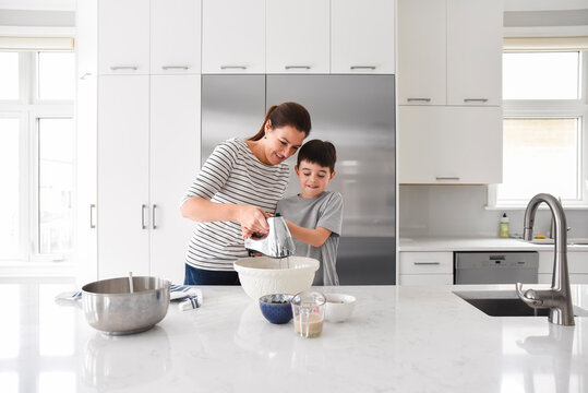 Mother helping young son use a mixer while cooking in a modern kitchen